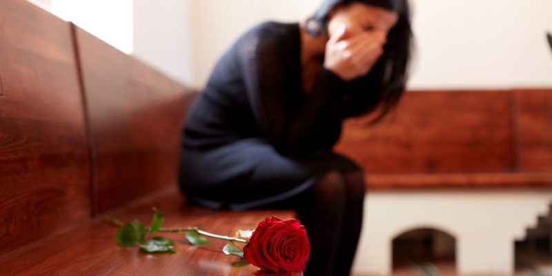 crying-woman-with-red-rose-at-funeral-in-church-95087754